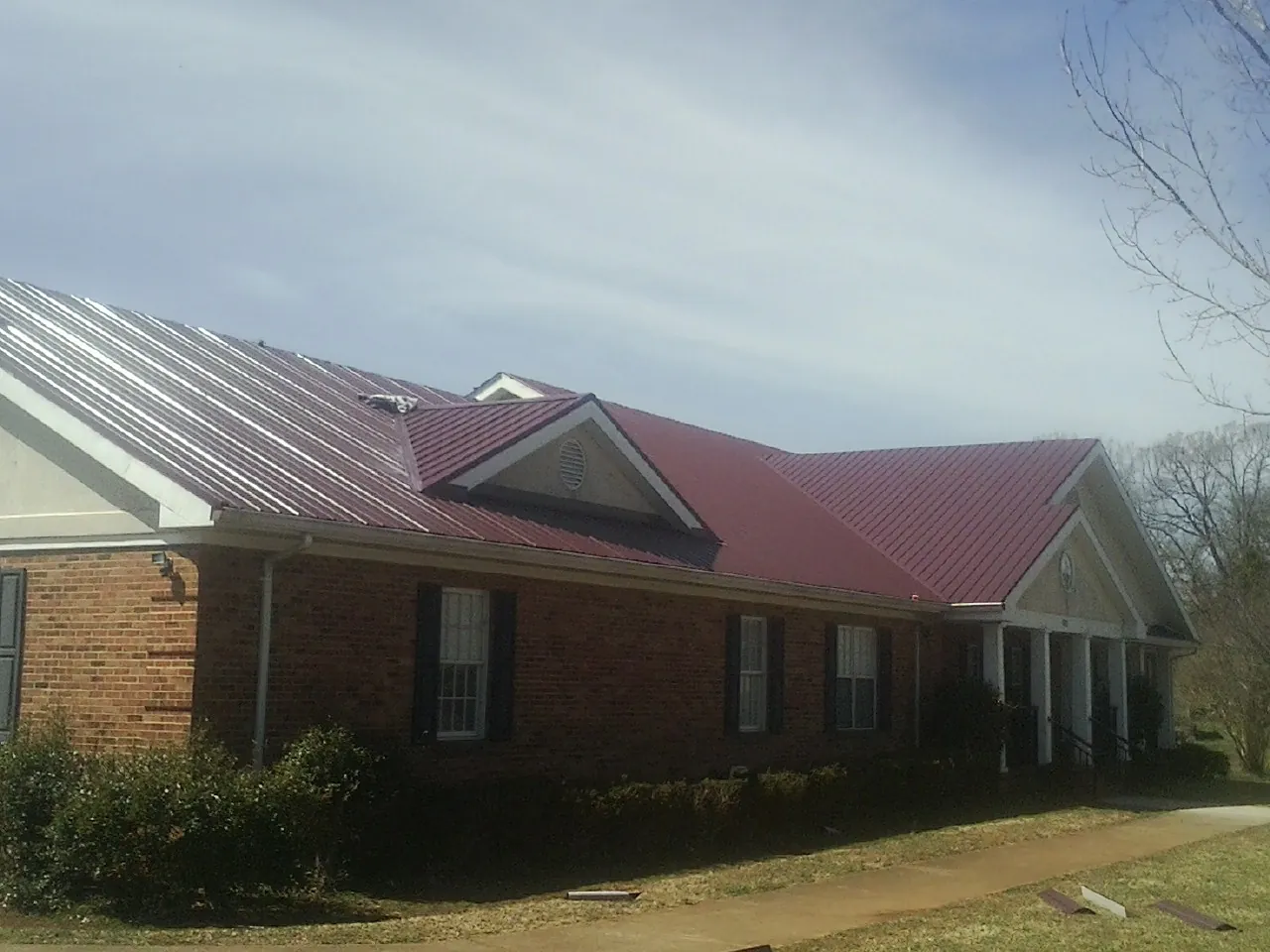 Red metal roof with gabled entries on a long brick building, from a Hail Damage Roof Repair job in Catawba